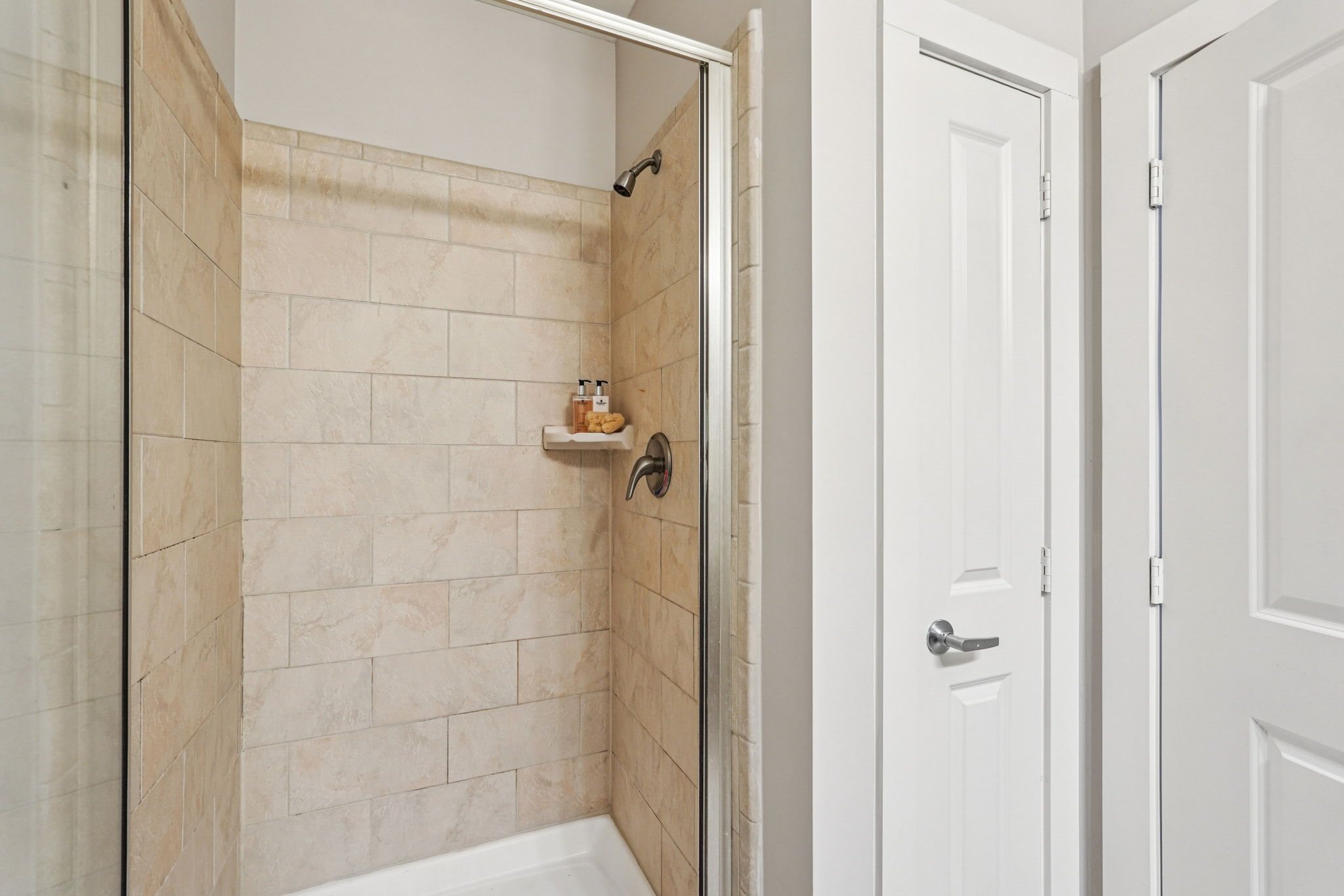 A white door is open to a bathroom with a tiled shower.